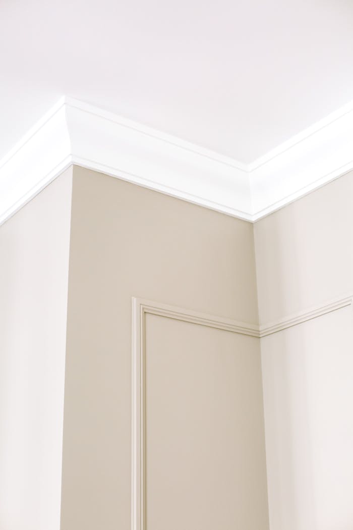 Close-up of intricate ceiling moulding and beige walls with minimalist design, showcasing home renovation details.